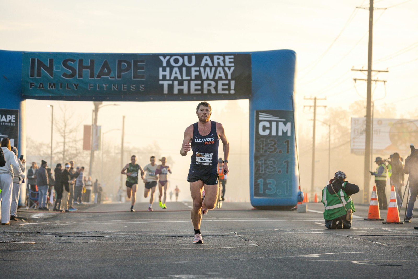 Why I Chose a Half Marathon (and the Brutal Reality of Training for One) Runner approaching the halfway mark in a marathon event with spectators and photographers capturing the moment.