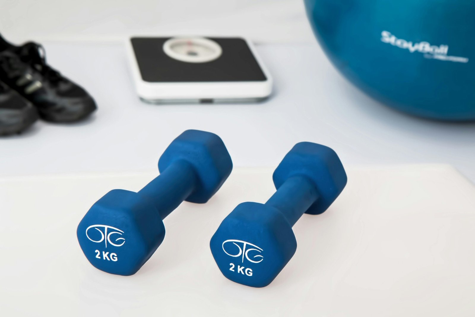 Why I Finally Started Strength Training (And Why You Probably Should Too) Blue dumbbells placed on a white surface with fitness equipment in the background.